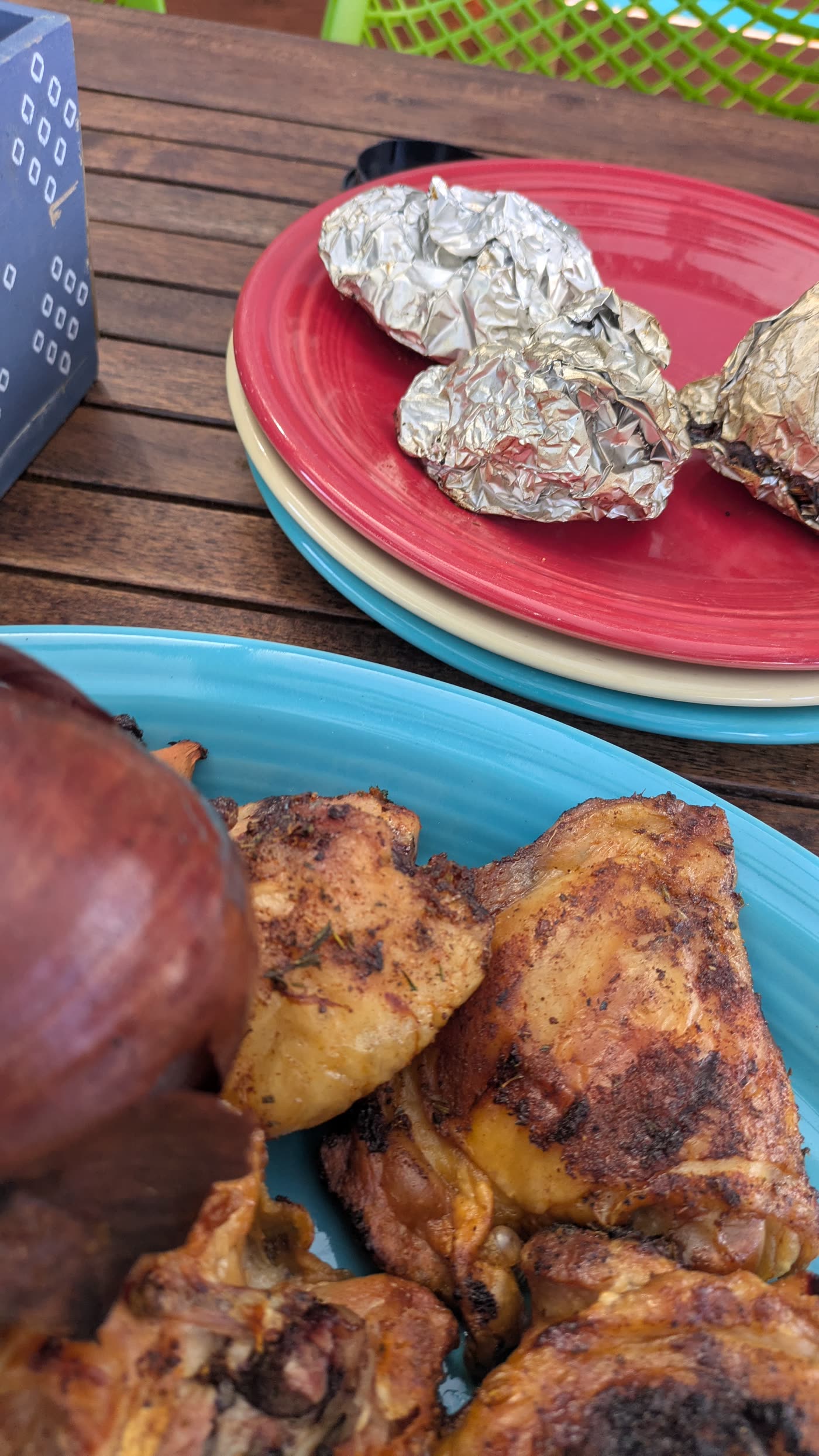 A red plate with foil-baked onions and garlic next to a blue plate of grilled chicken thighs on the dinner table