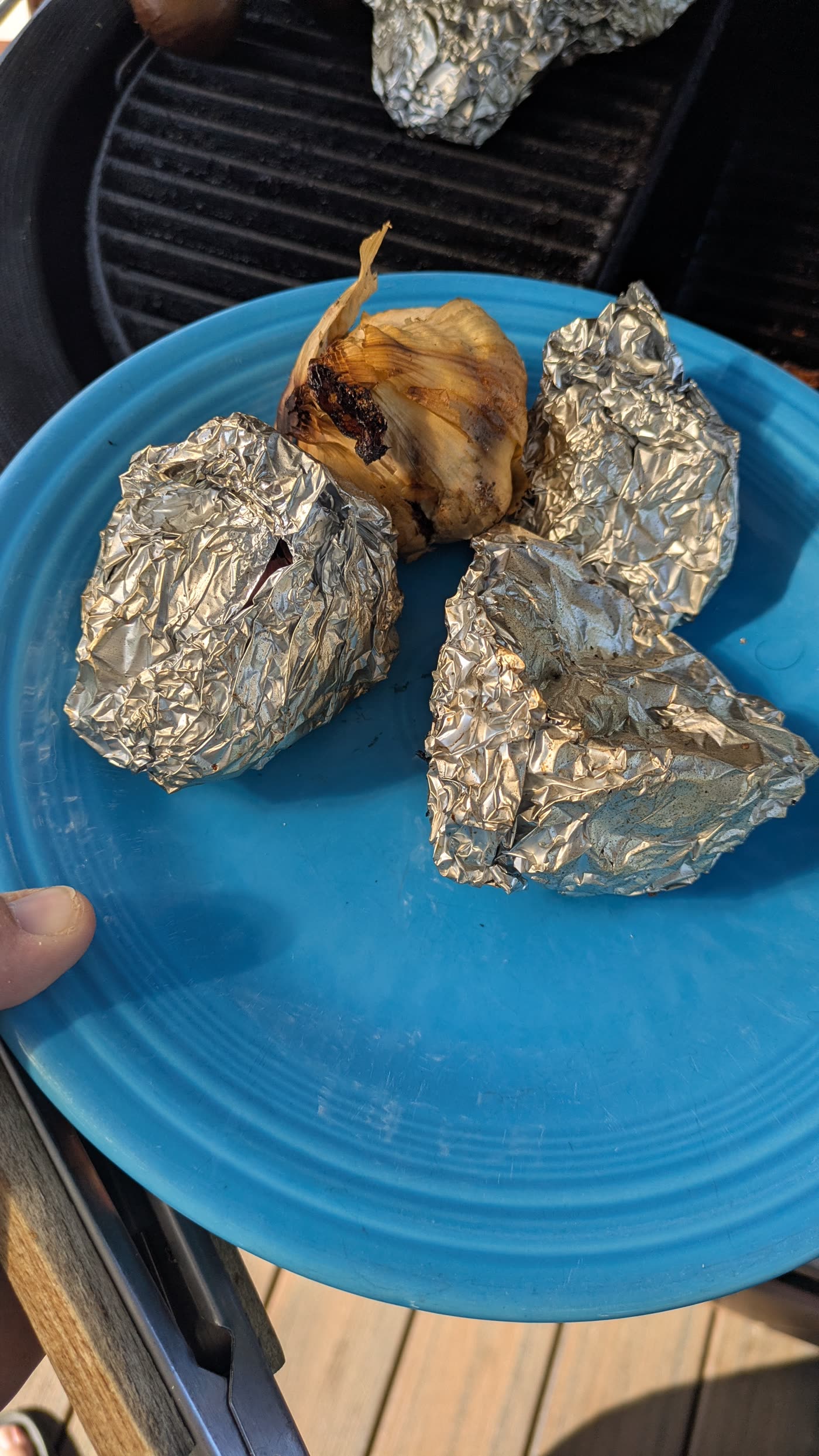 An unwrapped half-head of garlic with charred miso on the cut side, next to closed foil packs on a blue plate