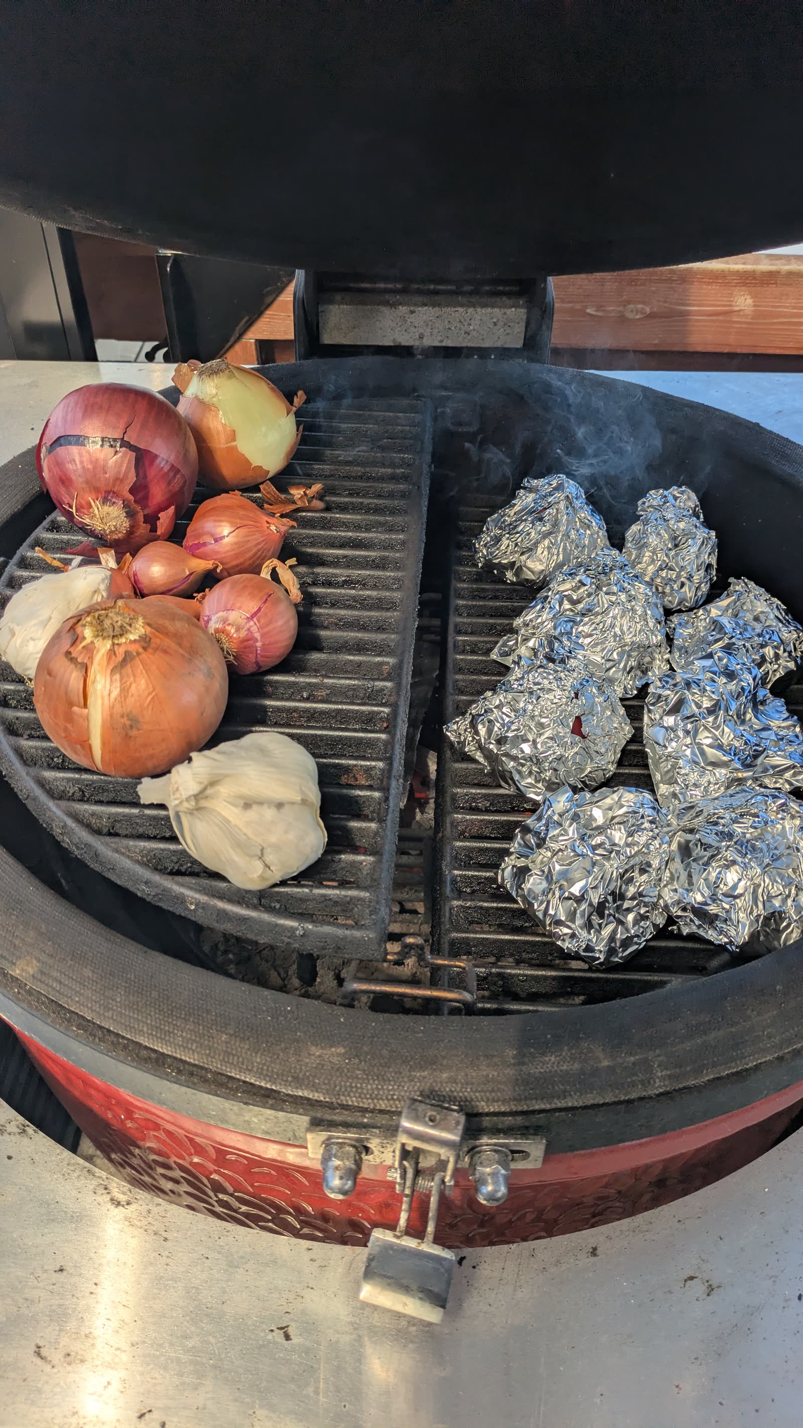 The Kamado Joe with whole onions on the left side of the grate and foil-wrapped garlic packs on the right