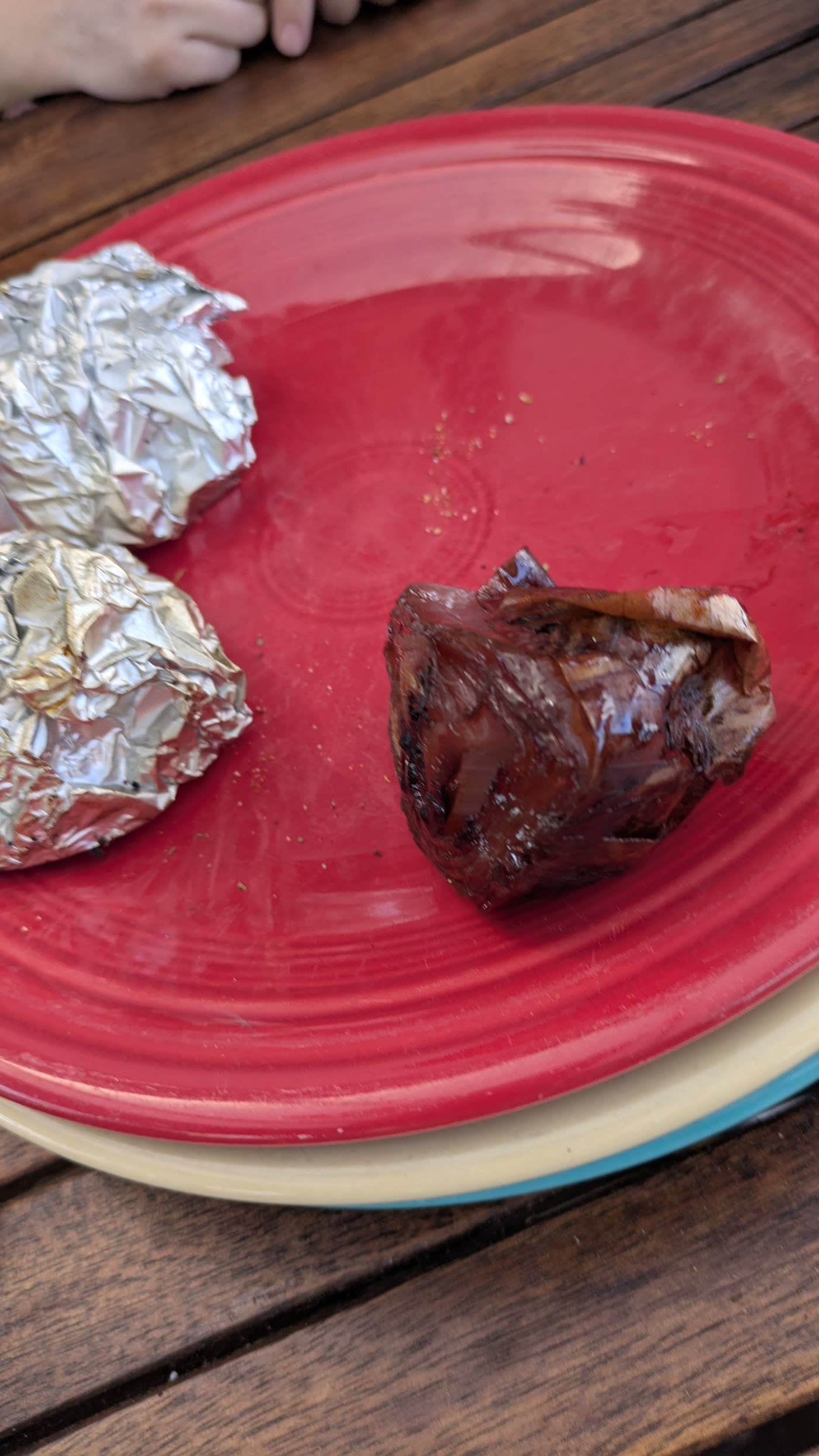 A caramelized whole onion next to foil packs from the cook