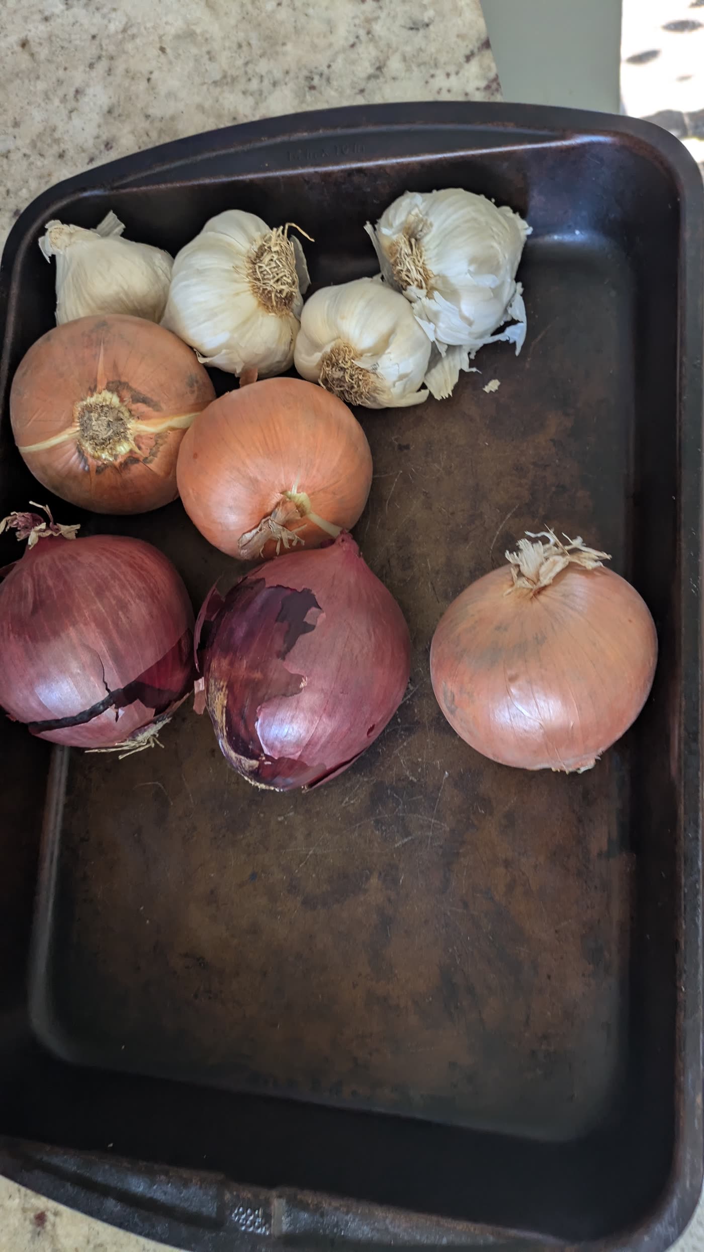 A black tray with four heads of garlic, three Spanish onions, and three red onions before prep